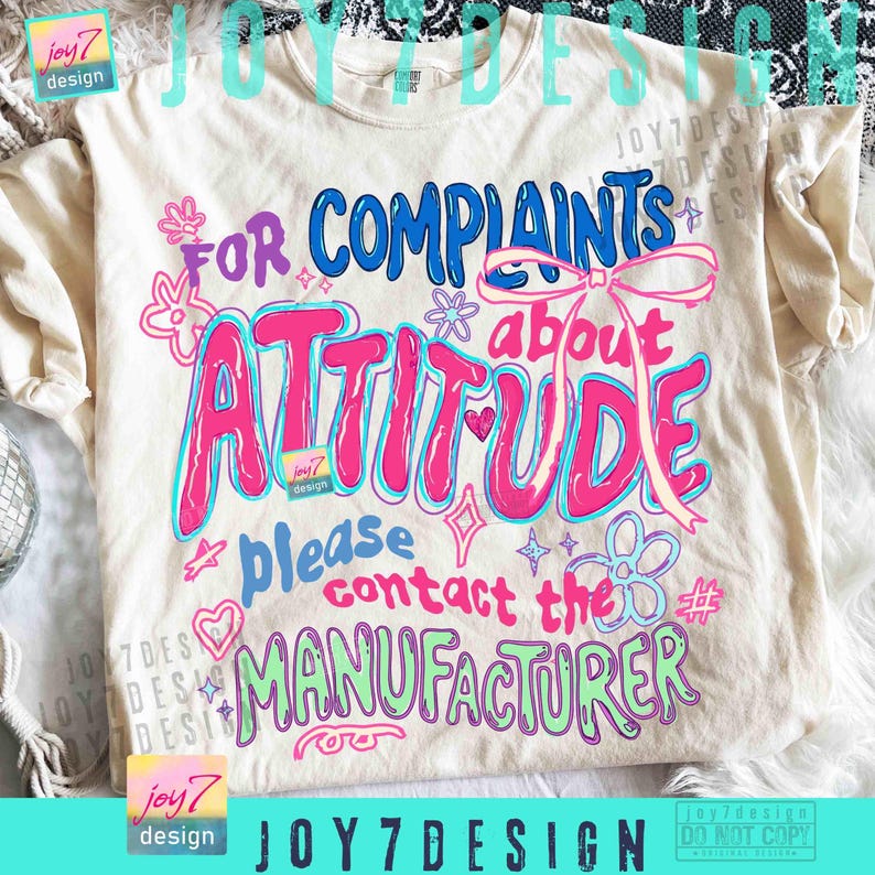 May include: Cream-colored t-shirt with the text "FOR COMPLAINTS ABOUT ATTITUDE please contact the MANUFACTURER" in blue, pink, and green. The design includes floral and heart accents.