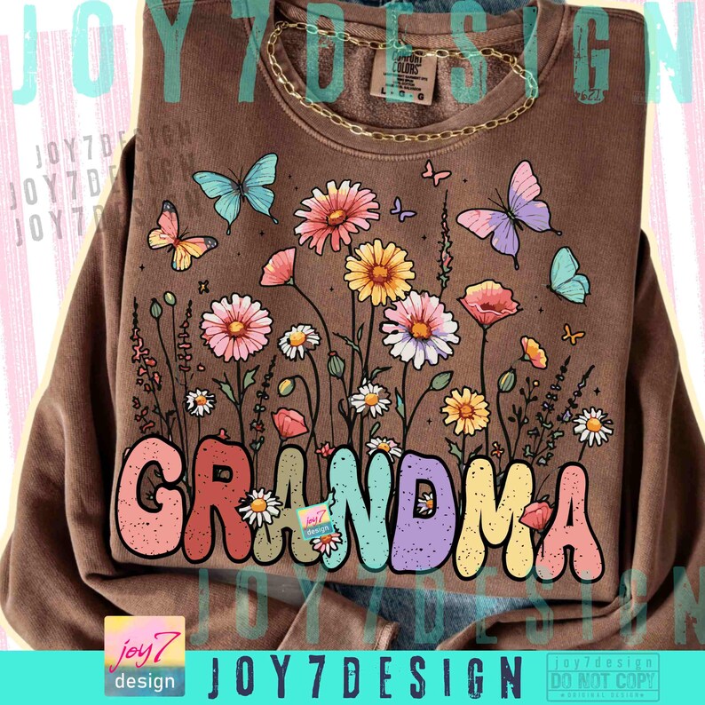 May include: Brown sweatshirt with a floral design and the word "GRANDMA" in colorful bubble letters. The design includes flowers and butterflies. A gold chain necklace is visible at the neckline. The sweatshirt has the text "JOY7DESIGN" at the bottom.