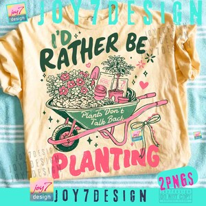 May include: A light yellow t-shirt with a gardening theme. The shirt features a graphic of a wheelbarrow filled with plants and the text "I'd Rather Be Planting". The design includes the text "Plants Don't Talk Back".