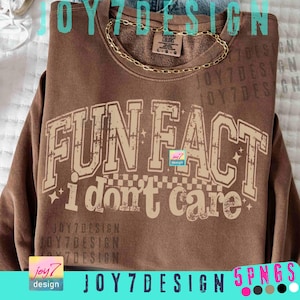 Puede incluir: Una sudadera marrón con el texto "FUN FACT i don't care" en una fuente desgastada de estilo universitario. La sudadera tiene cuello redondo y una cadena dorada. El diseño incluye estrellas y un patrón de cuadros.