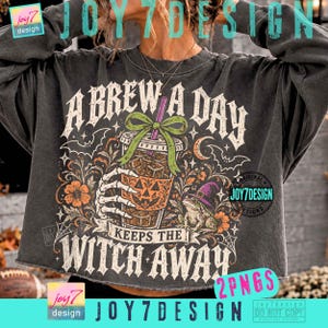 Può includere: Una felpa grigio antracite a maniche lunghe con una stampa grafica che riporta il testo A BREW A DAY KEEPS THE WITCH AWAY. Il design include una mano scheletrica che regge un caffè freddo a forma di zucca, un fiocco verde, una rana e pipistrelli.