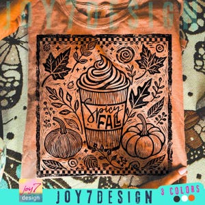 May include: Orange t-shirt with a black graphic design featuring a coffee cup with whipped cream, pumpkins, and leaves. The text "Spicy Fal" is written on the cup. The shirt is a fall-themed design.
