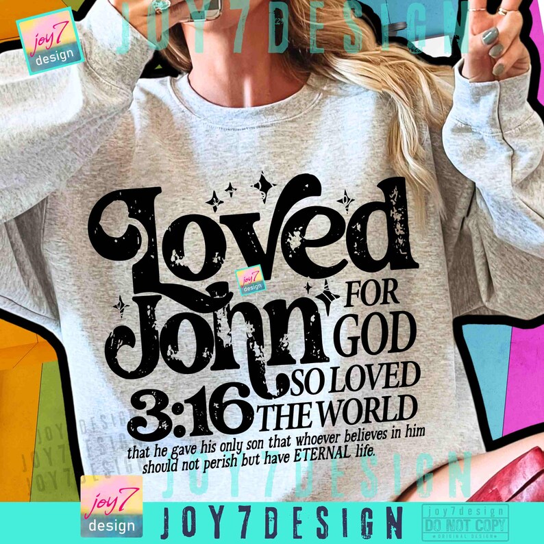 Op de afbeelding: Een lichtgrijs sweatshirt met de tekst "Loved For John 3:16 For God So Loved The World" in een zwarte, verweerde lettertype. Het sweatshirt bevat ook het vers "that he gave his only son that whoever believes in him should not perish but have ETERNAL life."