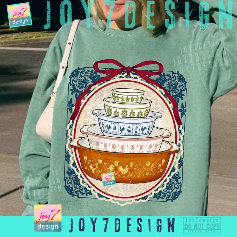 May include: A teal sweatshirt featuring a graphic of vintage Pyrex nesting bowls in various sizes and patterns. The design includes a red ribbon, a blue floral border, and the text "JOY7 DESIGN".