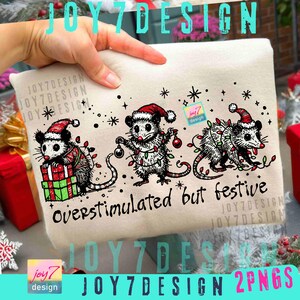 May include: A cream-colored tote bag featuring three opossums in Santa hats, decorated with Christmas lights and ornaments. The text "overstimulated but festive" is written in black script. The design includes snowflakes and the "JOY7DESIGN" logo.