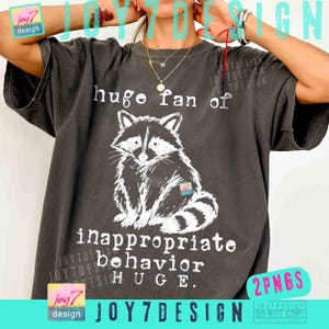 May include: Dark gray t-shirt featuring a white illustration of a raccoon and the text "huge fan of inappropriate behavior HUGE." The shirt has a vintage, worn look.