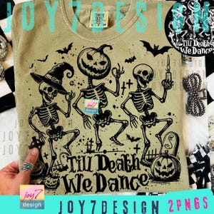 May include: A light olive green t-shirt featuring a black graphic of three dancing skeletons, one with a witch hat, one with a pumpkin head, and one holding a candle. The text "Till Death We Dance" is below the skeletons. Bats and pumpkins are also in the design.