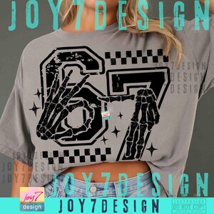 Peut inclure: T-shirt gris avec un motif noir du chiffre 67, repr&eacute;sentant des mains de squelette. Le motif comprend un motif &agrave; carreaux et des &eacute;toiles. Le texte "JOY7DESIGN" est visible.