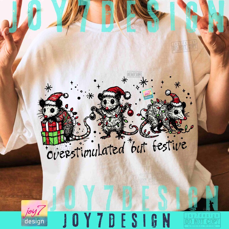 Puede incluir: Camiseta blanca con tres zarig&uuml;eyas de dibujos animados con gorros de Pap&aacute; Noel y luces navide&ntilde;as. Las zarig&uuml;eyas sostienen regalos y adornos. El texto "overstimulated but festive" est&aacute; impreso debajo.