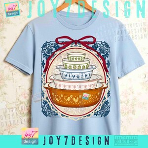 May include: Light blue t-shirt featuring a graphic of vintage casserole dishes in various sizes and patterns. The design includes a red ribbon and a decorative blue and white border. The shirt has the text "JOY7DESIGN".