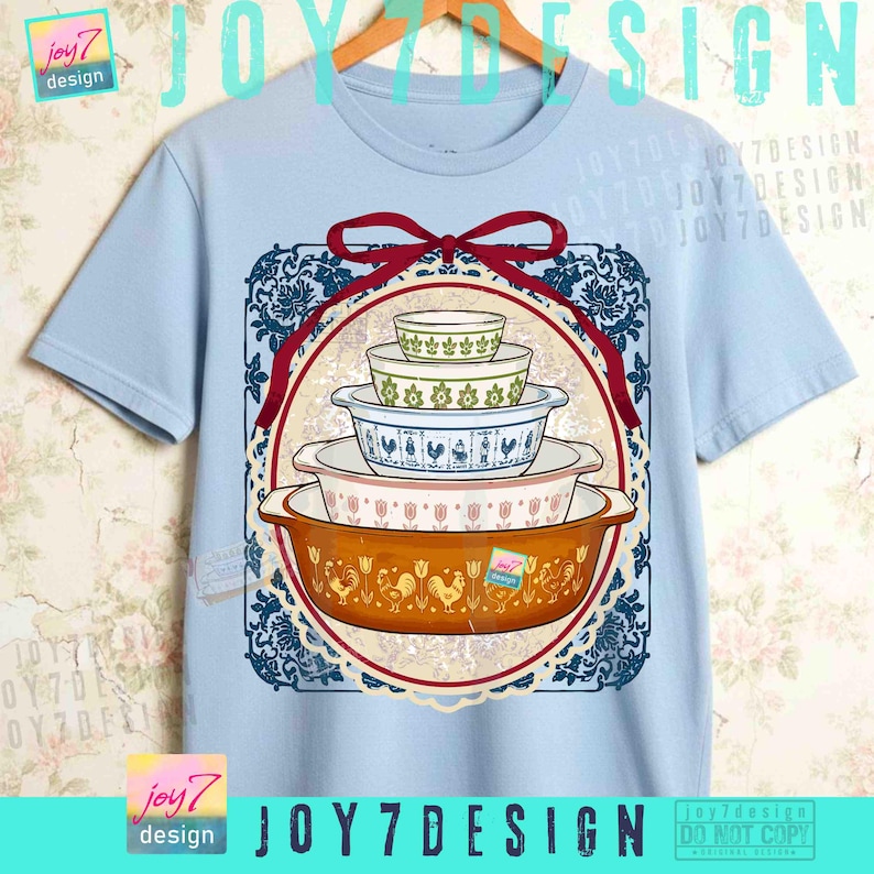 May include: Light blue t-shirt featuring a graphic of vintage casserole dishes in various sizes and patterns. The design includes a red ribbon and a decorative blue and white border. The shirt has the text "JOY7DESIGN".