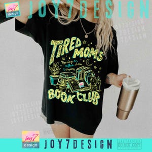 May include: Black t-shirt featuring a neon green and yellow graphic. The graphic says "Tired Moms Book Club" with illustrations of books, plants, and candles. The text "Running on coffee, chaos & chapters" is also included.