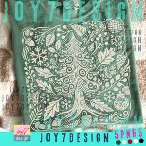 May include: A sage green t-shirt featuring a detailed white graphic of a tree with leaves, snowflakes, and acorns. The text "JOY7 DESIGN" is printed on the shirt. The shirt is made of a soft material.