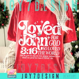 Op de afbeelding: Een rood t-shirt met de woorden "Loved John 3:16 For God So Loved The World" in witte letters. De tekst bevat de zin "dat hij zijn eniggeboren Zoon gegeven heeft, opdat een ieder die in hem gelooft, niet verloren gaat, maar eeuwig leven heeft."