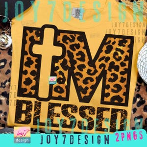 May include: Mustard yellow t-shirt with the words "I'M BLESSED" in black. The letters "I" and "M" are filled with a leopard print pattern. A cross shape is in the letter "I". The shirt has a Comfort Colors tag.