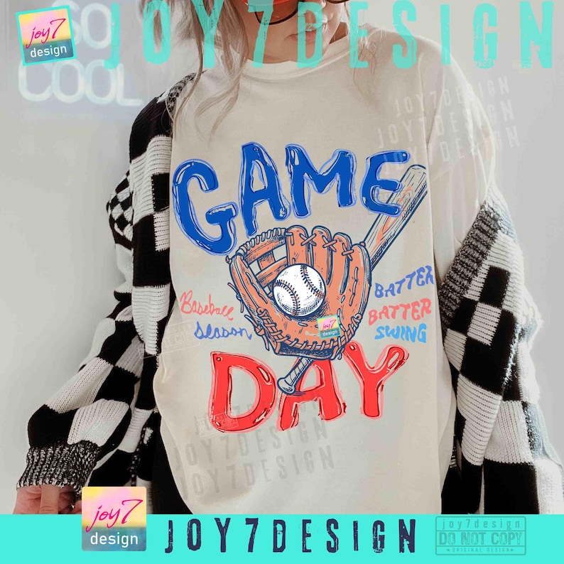 May include: Cream-colored t-shirt with a baseball-themed graphic. The design features the words "GAME DAY" in blue and red, a baseball glove, a baseball, and a bat. The words "Baseball Season", "Batter, Batter, Swing" are also included.