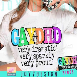 May include: White t-shirt with the text "GAYDHD" in rainbow colors. Below the text are the words "very dramatic, very sparkly, very proud" in a black font. The shirt has a design by Joy7 Design.