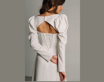 May include: A white long-sleeved dress with a fitted bodice and a flowing skirt. The bodice has a keyhole cutout in the back and a lace-up detail.