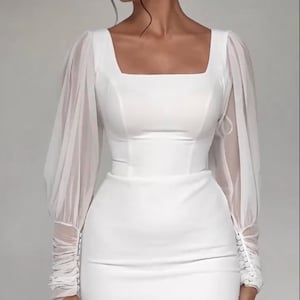 Pode incluir: Um vestido branco com mangas compridas e decote quadrado. As mangas s&atilde;o feitas de um tecido transparente e t&ecirc;m um detalhe franzido nos punhos.