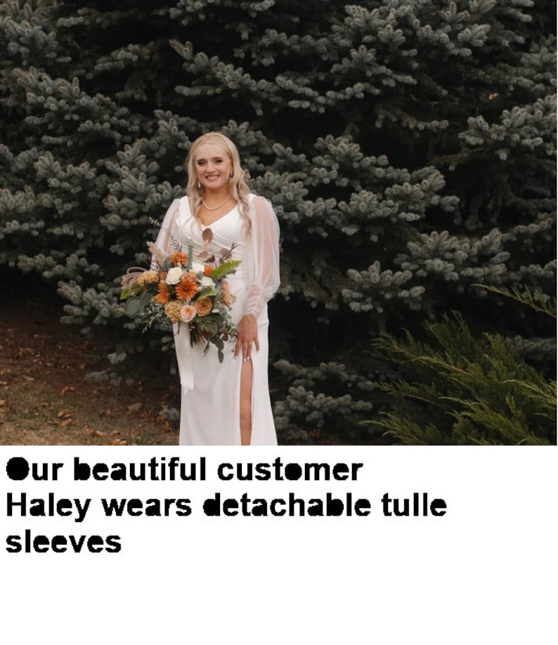 Pode incluir: Uma mulher com um vestido de noiva branco com uma fenda na saia e mangas de tule posa em frente a uma &aacute;rvore verde de folha perenne. Ela est&aacute; segurando um buqu&ecirc; de flores.
