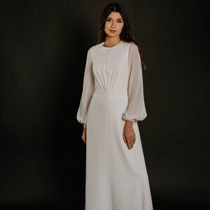 May include: A white long-sleeved dress with a round neckline and a button fastening. The dress has a fitted bodice and a flowing skirt.