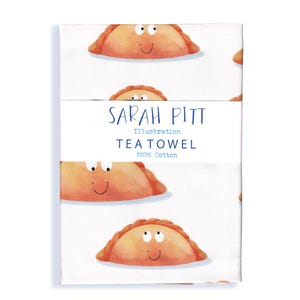 May include: A white cotton tea towel featuring a repeating pattern of orange, semi-circular pastry illustrations with cartoon faces. A central paper band displays the text SARAH PITT Illustration TEA TOWEL 100% Cotton in blue lettering.