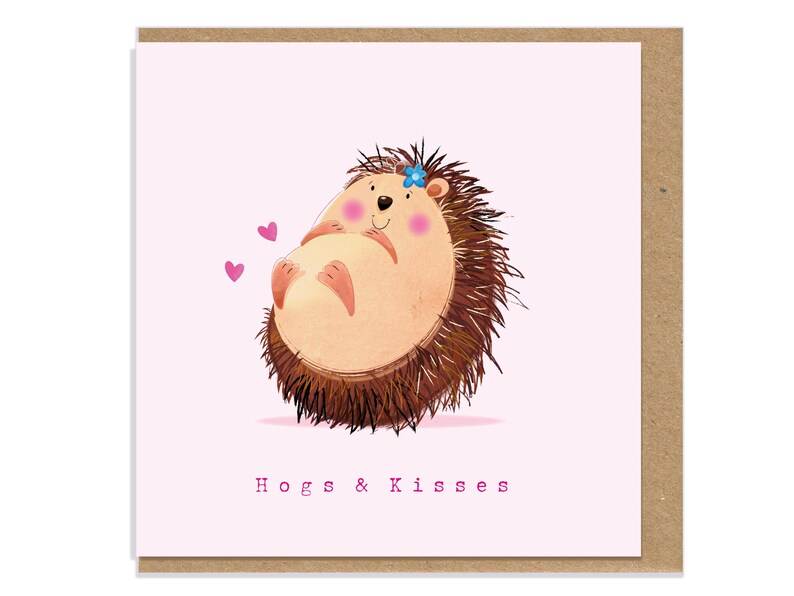 May include: A square greeting card with a light pink background featuring a cartoon hedgehog with a blue flower on its head, pink cheeks, and two small pink hearts. The text "Hogs & Kisses" is printed in pink at the bottom of the card.