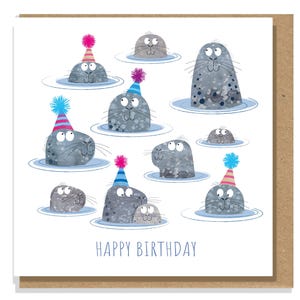 May include: A square birthday card with a brown border. The card features cartoon seals in water, wearing party hats. The seals are grey with white eyes and whiskers. The words "HAPPY BIRTHDAY" are written in blue at the bottom.