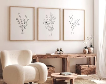 May include: Three framed black and white line drawings of floral bouquets. The drawings are in simple, minimalist style. The frames are light wood and are hung on a white wall.