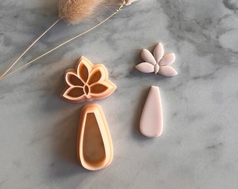 May include: Two pink plastic cookie cutters, one shaped like a flower and the other shaped like a teardrop. The flower cutter has a smaller flower cutout in the center.