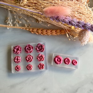 May include: A set of two clear silicone moulds for making resin flower charms. The moulds are filled with pink resin flowers. The larger mould has nine flower cavities and the smaller mould has three flower cavities.