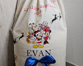 May include: A cream-coloured drawstring gift bag with a Disney character design. The bag has a blue ribbon and the name "EVAN" printed in black. The text "LIAISON SPÉCIALE POUR:" is printed in red.