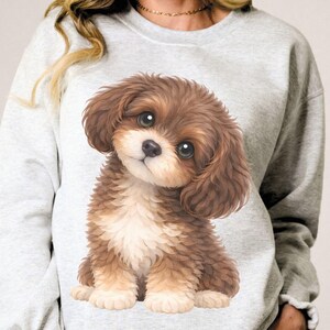 May include: Light gray sweatshirt featuring a detailed illustration of a puppy. The puppy has brown and tan fur, large eyes, and a sweet expression. The sweatshirt is a casual style, perfect for everyday wear.