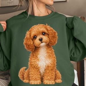 Op de afbeelding: Een donkergroene sweatshirt met een gedetailleerde illustratie van een lichtbruine puppy. De puppy heeft een witte borst en zit rechtop. De sweatshirt is effen van kleur, met de puppy-illustratie gecentreerd op de voorkant.