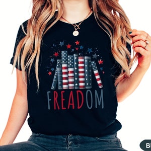 May include: Black t-shirt with a graphic of stacked books with an American flag design and the word "FREEDOM" in red, white, and blue.