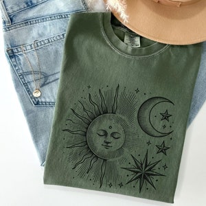 May include: A green t-shirt with a black sun, moon, and stars graphic. The text "Moss" is visible in the bottom right corner of the image.