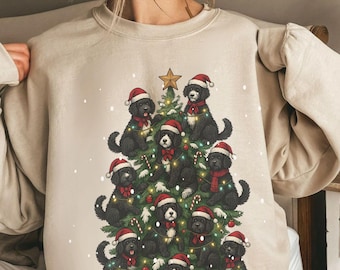 Könnte beinhalten: Sandfarbenes Sweatshirt mit einem Weihnachtsbaum-Design aus schwarzen Hunden mit Weihnachtsmützen und roten Schals. Der Baum ist mit Lichterketten, Zuckerstangen und einem goldenen Stern geschmückt. Ein festliches Kleidungsstück zum Thema Feiertage.