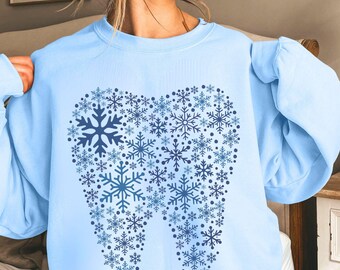 May include: Light blue sweatshirt featuring a tooth design made up of snowflakes. The tooth is outlined in blue and filled with blue snowflakes.