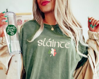 May include: A moss green oversized t-shirt with the Irish phrase "sláinte" and a shamrock with the Irish flag colors printed on the front.