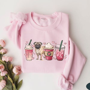 May include: Pink sweatshirt with a graphic of a pug dog and three iced coffee drinks with hearts. The drinks are labeled with hearts and the text "Love"