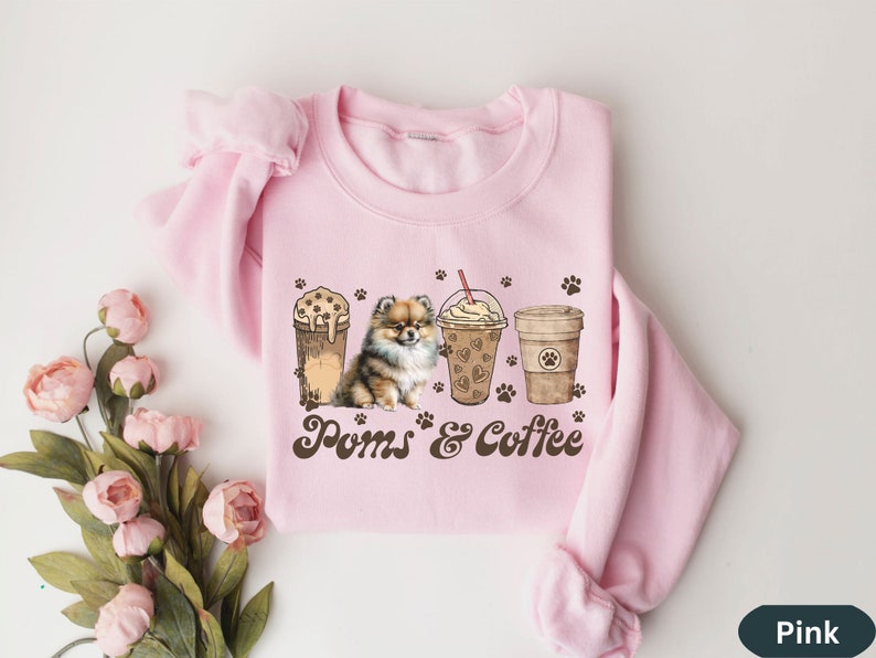Puede incluir: Sudadera rosa con un gr&aacute;fico marr&oacute;n de un perro pomerania, dos tazas de caf&eacute; y el texto "Poms & Coffee".