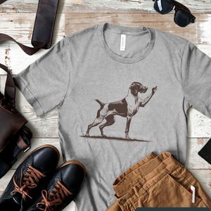May include: A gray t-shirt with a black and white illustration of a dog giving the middle finger. The text "Athletic Heather" is printed on the bottom of the shirt.