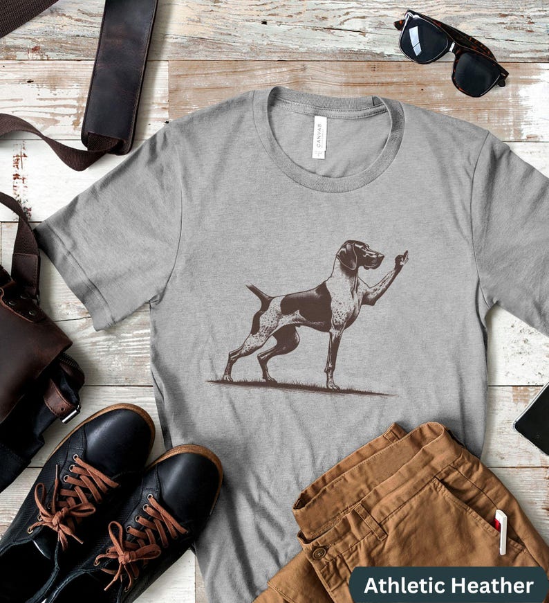 May include: A gray t-shirt with a black and white illustration of a dog giving the middle finger. The text "Athletic Heather" is printed on the bottom of the shirt.