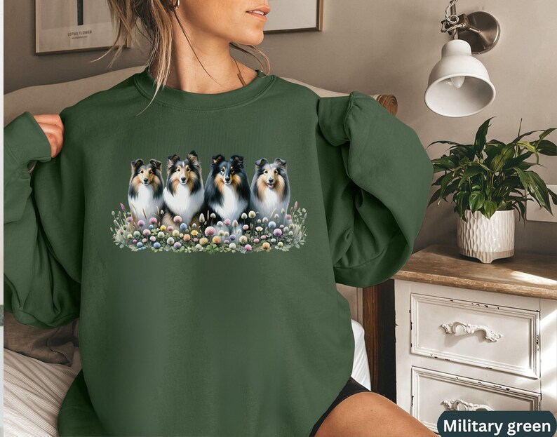 Puede incluir: Una sudadera verde con un gr&aacute;fico de cuatro perros Collie en un campo de flores. Los perros son negros y blancos con ojos marrones. Las flores son rosas, moradas y amarillas.