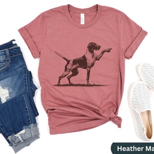 Pu&ograve; includere: T-shirt color malva heather con un'illustrazione grafica marrone di un Bracco tedesco a pelo corto che punta.