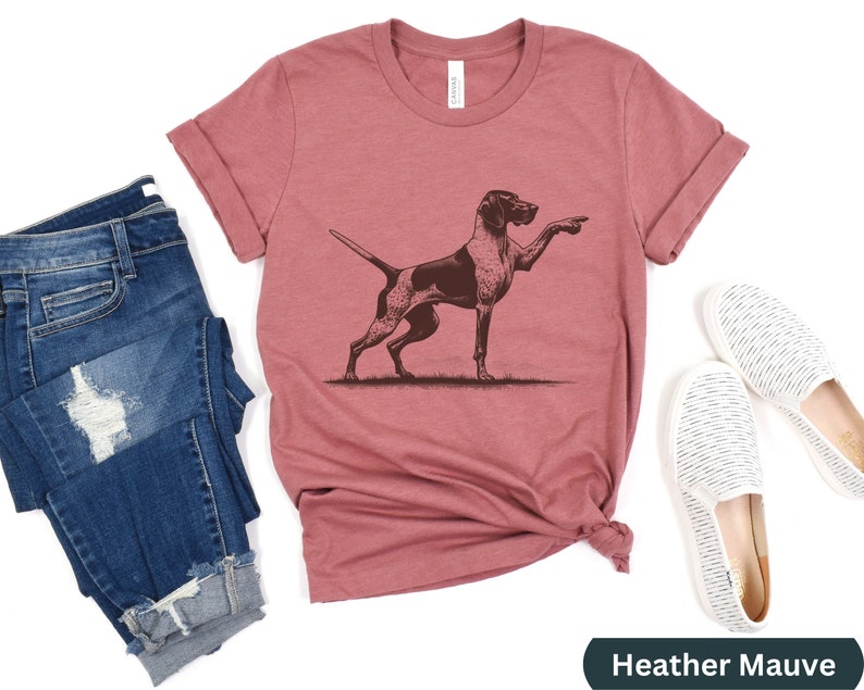 Pu&ograve; includere: T-shirt color malva heather con un'illustrazione grafica marrone di un Bracco tedesco a pelo corto che punta.