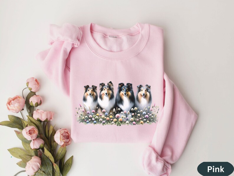 Puede incluir: Sudadera rosa con un gr&aacute;fico de cuatro Shetland Sheepdogs sentados en un campo de flores.