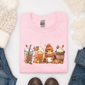 May include: Pink sweatshirt with a graphic of a squirrel holding a cup of coffee and surrounded by fall leaves and pumpkins. The text "Gilded" is visible on the tag.