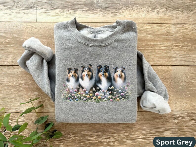 Puede incluir: Una sudadera gris con un estampado de cinco perros Collie en un campo de flores. Los perros miran todos a la c&aacute;mara y tienen pelo negro y blanco.