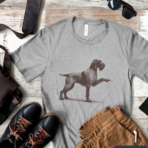 May include: A grey t-shirt with a black and white illustration of a German Shorthaired Pointer dog. The dog is standing with its right paw raised. The text "Sport Grey" is visible at the bottom of the image.